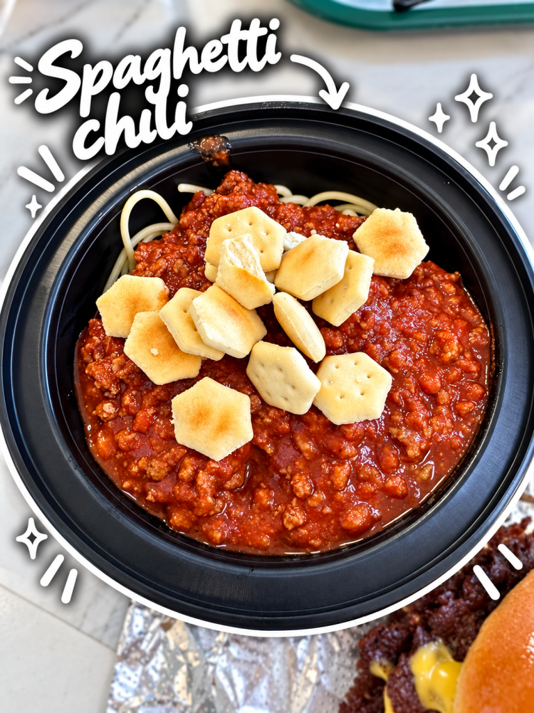 A bowl of spaghetti chili topped with crackers, featuring a rich meat sauce and noodles.
