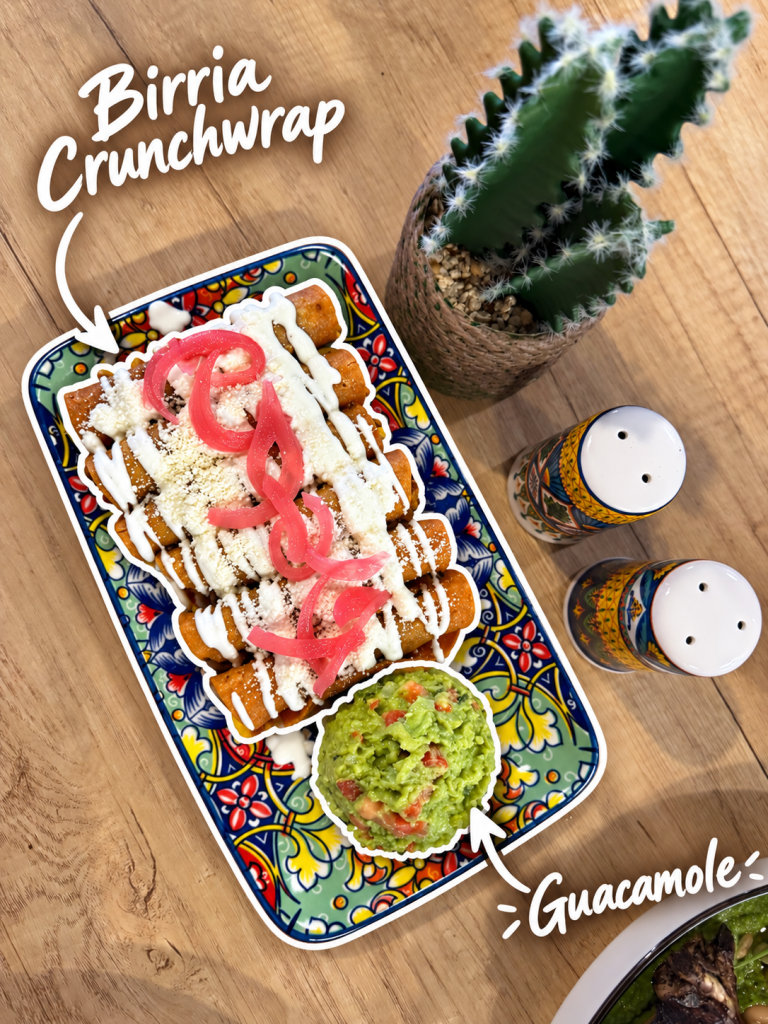 A colorful platter featuring Birria Crunchwrap topped with crema, onions, and cheese, accompanied by a bowl of guacamole and decorated with a small cactus and decorative salt shakers.