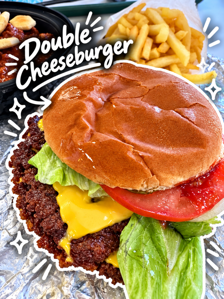 A juicy double cheeseburger with melted cheese, lettuce, and tomato, accompanied by a side of fries and a dish of chili.