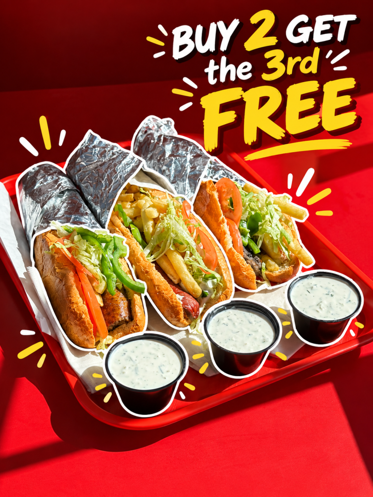 Three wrapped hot dogs with lettuce, tomato, and fries on a red tray, accompanied by two cups of dipping sauce, with a promotional banner that states 'Buy 2 Get the 3rd Free'.