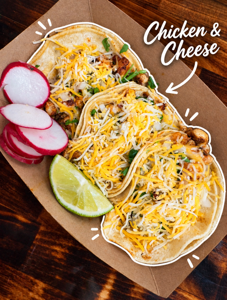 Three chicken and cheese tacos garnished with shredded cheese, chopped onions, and cilantro, served with lime wedges and sliced radishes.