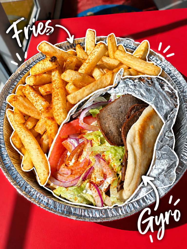 A foil container filled with seasoned fries and a gyro wrapped in foil, accompanied by lettuce, tomatoes, onions, and sauce.