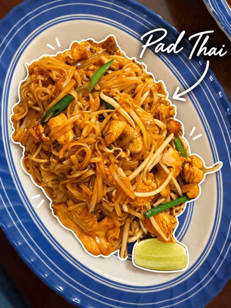 A vibrant plate of Pad Thai featuring stir-fried rice noodles with chicken, bean sprouts, and green onions, garnished with a lime wedge.