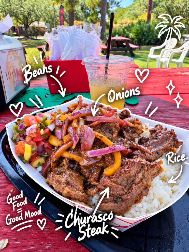 A vibrant plate of Churrasco steak served over rice, accompanied by beans, onions, and a fresh salsa. In the background, a picnic area with red tables and a drink with a straw.